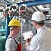 Arbeiter mit Schutzhelmen in Industrieanlage inspizieren einen tragbaren Bildschirm