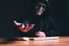 Black hat hacker force demands ransom by holding out his hand on table where sensitive data is hacked in a dark room in the background. Cyber security and cyber crime concept. Hacking and phishing