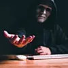 Black hat hacker force demands ransom by holding out his hand on table where sensitive data is hacked in a dark room in the background. Cyber security and cyber crime concept. Hacking and phishing