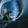 Professional Heavy Industry Welder Working Inside Pipe, Wears Helmet and Starts Welding. Construction of the Oil, Natural Gas and Fuels Transport Pipeline. Industrial Manufacturing Factory