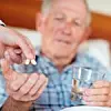 Älterer Mann im Bett der Wasserglas hält und Tabletten gereicht bekommt