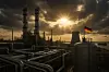 Ein riesiges, modernes Industrieareal mit Chemie- und Pharmaanlagen im Vordergrund, darunter glänzende Rohrleitungen, Reaktoren und hohe Kühltürme mit leichtem Dampf. Die Sonne bricht dramatisch durch dunkle, noch bedrohlich wirkende Wolken – Symbol für die überraschend positive Entwicklung im ersten Quartal 2025, aber auch die eingetrübten Erwartungen. Im Hintergrund ist ein Frachtschiff im Hafen zu sehen (symbolisch für internationale Handelsbeziehungen). Eine Deutschlandflagge auf einem Kran oder einer Anlage verweist dezent auf den Standort.