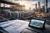 Tablet mit Anlagenansicht und ausgerollten Bauplänen vor einer weitläufigen Industrieanlage.