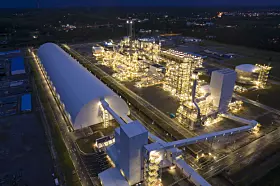 Beleuchtete Industrieanlage mit Lagerhalle und Rohrleitungen in der Nachtluftaufnahme