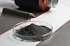 Schwarzes Pulver in Petrischale vor beschichteten Batterie-Metallfolien