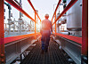 Arbeiter in blauer Schutzkleidung geht über Steg in Industrieanlage bei Sonnenuntergang