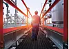 Arbeiter in blauer Schutzkleidung geht über Steg in Industrieanlage bei Sonnenuntergang