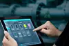 Hand bedient Siemens‑Tablet zur Überwachung einer Industrieanlage im Hintergrund.