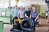 Gruppe von Mitarbeitern steht in einer Werkhalle hinter einem großen Industriegebläse.