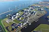 Luftaufnahme eines Industriegebiets an der Küste mit Windrädern, Straßen und Wasserflächen.