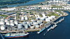 Luftaufnahme eines Industriehafens mit großen Tanks, Pipelines, Kaianlagen und Schiffen am Wasser.