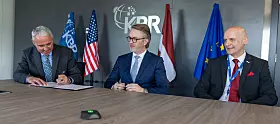 Drei Männer an einem Tisch vor Flaggen bei einem offiziellen Gespräch.