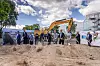 Spatenstich bei KSB vor einem Hochregal mit Bagger und mehreren Personen auf einer Baustelle.