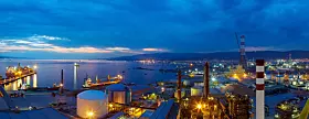 Blick auf einen Industriehafen mit Kränen, Schiffen und Lichtern bei Dämmerung.
