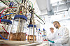 Forscher im Labor neben Glasreaktoren und technischen Leitungen in einer Biotechnologie-Anlage.