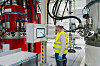 Arbeiter in Warnweste steht vor einem Bedienpanel in einer Industrieanlage mit Tanks und Rohren.