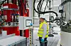 Arbeiter in Warnweste steht vor einem Bedienpanel in einer Industrieanlage mit Tanks und Rohren.