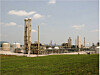 Industrieanlage mit Türmen, Tanks und Rohrleitungen hinter einer grünen Wiese.