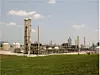 Industrieanlage mit Türmen, Tanks und Rohrleitungen hinter einer grünen Wiese.