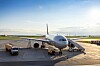 Passagierflugzeug auf einem sonnigen Flughafen-Vorfeld mit Servicefahrzeug daneben.