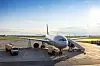 Passagierflugzeug auf einem sonnigen Flughafen-Vorfeld mit Servicefahrzeug daneben.