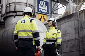 Zwei Personen in Schutzkleidung stehen vor einer Industrieanlage mit Yara-Logo.