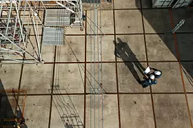 Blick von oben auf eine Baustelle mit Gerüsten und zwei Arbeitern auf dem Betonboden.