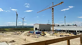 Windräder neben einer großen Industriebaustelle mit Kran und Bauzubehör unter blauem Himmel.