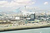 Blick über ein Hafengebiet mit Industrieanlagen, Kränen und Wasser bei hellem Tageslicht.