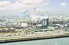 Blick über ein Hafengebiet mit Industrieanlagen, Kränen und Wasser bei hellem Tageslicht.