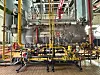 Komplexe Industrieanlage mit gelben Rohren, Ventilen und Stahlgerüst in einer Produktionshalle.