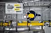 Person in Schutzkleidung kontrolliert gelbe Rohrleitung und Armaturen in einer Industrieanlage von oben.