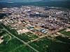 Luftaufnahme eines großen Industriekomplexes mit Hallen, Tanks und Rohrleitungen inmitten von Grünflächen.