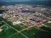 Luftaufnahme eines großen Industriekomplexes mit Hallen, Tanks und Rohrleitungen inmitten von Grünflächen.