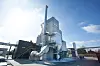 Industrieanlage mit silbernen Rohren und hohen Metallstrukturen bei blauem Himmel.