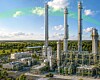 Große Industrieanlage mit hohen Metalltürmen und Rohrleitungen in einer offenen Landschaft.