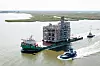 Großes Industrie-Modul auf einem Lastkahn, begleitet von Schleppern auf dem Wasser.