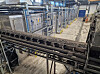 Förderanlage mit Metallgestellen und Rohrleitungen in einer Produktionshalle.