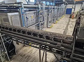 Förderanlage mit Metallgestellen und Rohrleitungen in einer Produktionshalle.