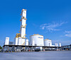 Weiße Industrietanks und Anlagenrohre vor blauem Himmel auf einem Werksgelände.
