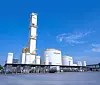 Weiße Industrietanks und Anlagenrohre vor blauem Himmel auf einem Werksgelände.