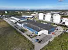 Luftbild einer Industrieanlage mit mehreren weißen Tanks, Hallen und Zufahrtswegen.