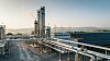 Industrieanlage mit Rohrleitungen, hohem Turm und Solarpanels im Vordergrund.