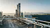 Industrieanlage mit Rohrleitungen, hohem Turm und Solarpanels im Vordergrund.