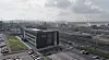 Weitwinkelansicht eines Industriegebiets mit Bürogebäude, Straßen und Hafen im Hintergrund.