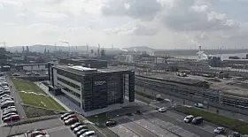 Weitwinkelansicht eines Industriegebiets mit Bürogebäude, Straßen und Hafen im Hintergrund.