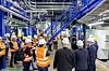 Gruppe von Personen mit Schutzhelmen und Warnwesten in einer Industrieanlage neben einer blauen Treppe.
