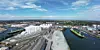 Luftbild eines Industriehafens mit Schiffen, Kränen und Lagerhallen am Wasser.