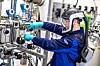 Techniker mit Helm und Handschuhen arbeitet an Rohrleitungen und Ventilen in einer Industrieanlage.
