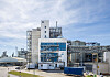 Große Industrieanlage mit Gebäuden, Rohrleitungen und Metallkonstruktionen bei klarem Himmel.